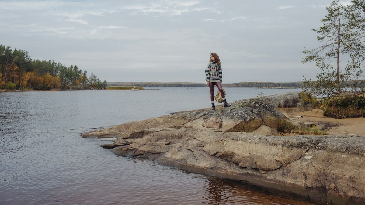 man in red and white plaid shirt standing on brown rock near body of water during